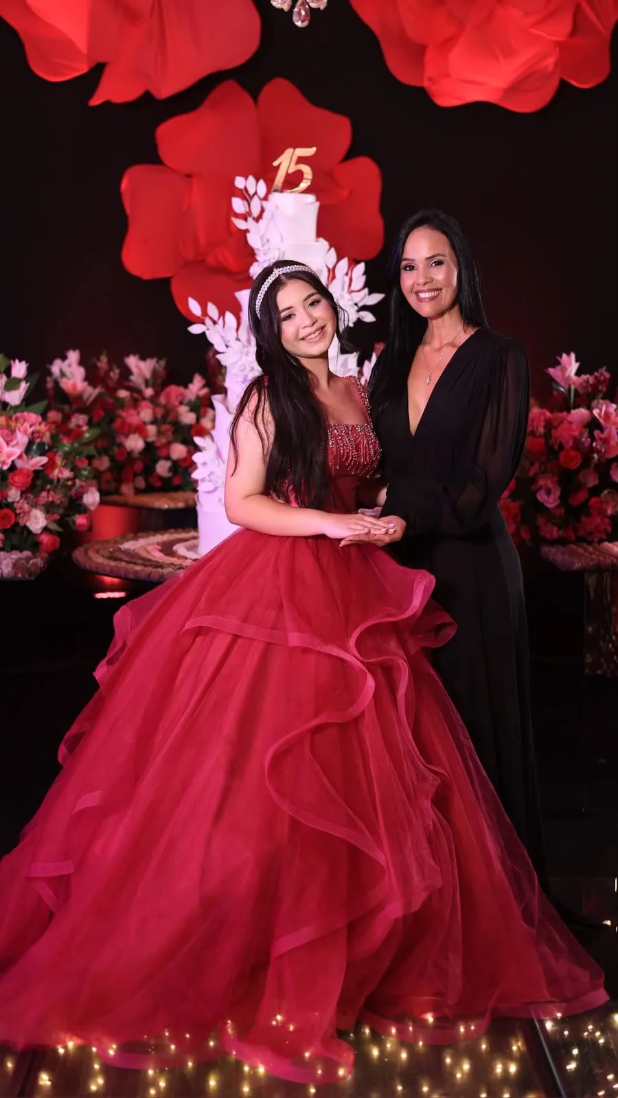 Debutante e Cris diante do bolo de três andares e flores vermelhas