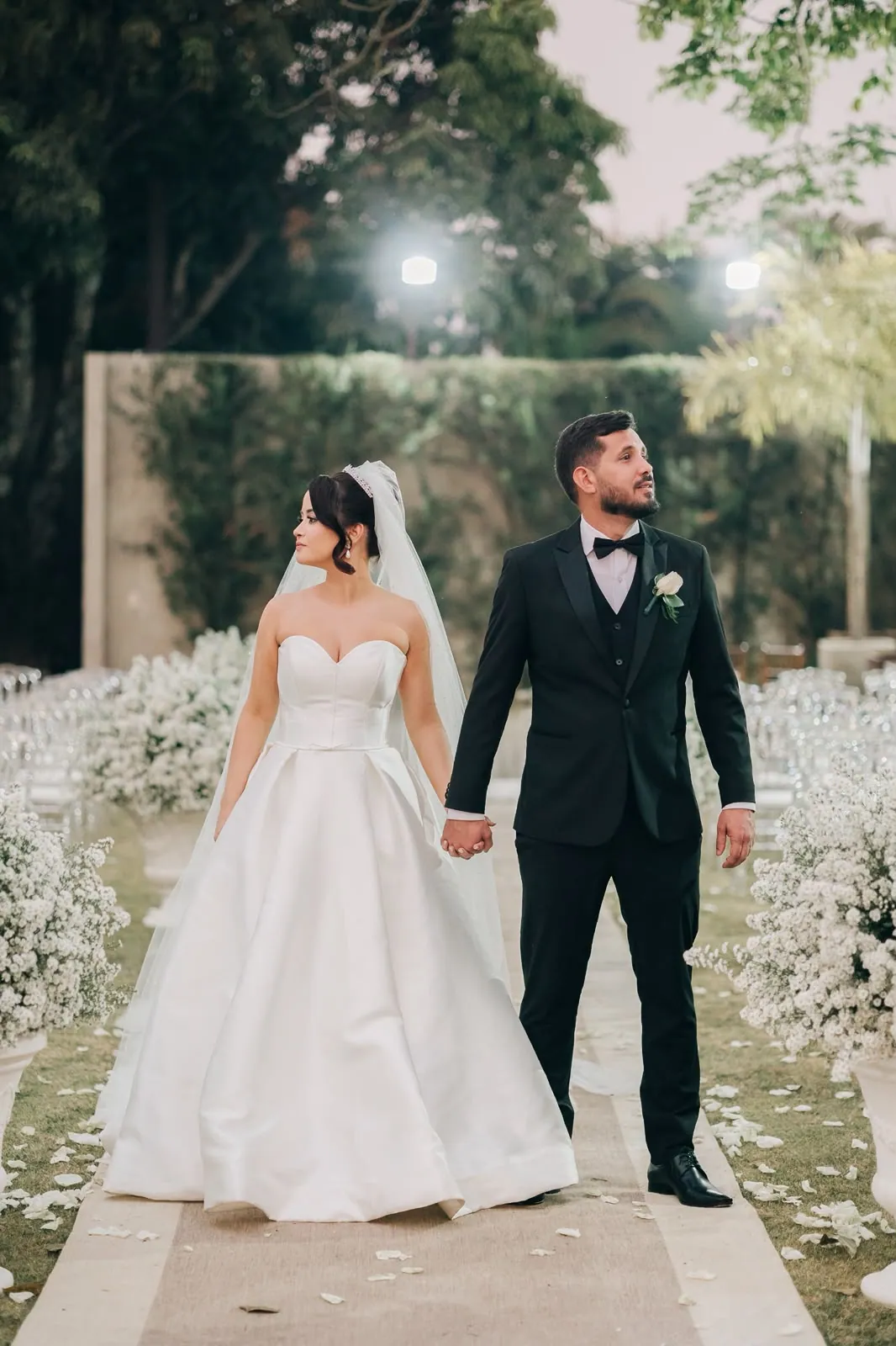Noivos de mãos dadas em corredor de mosquitinho ao entardecer, casamento clássico em Brasília