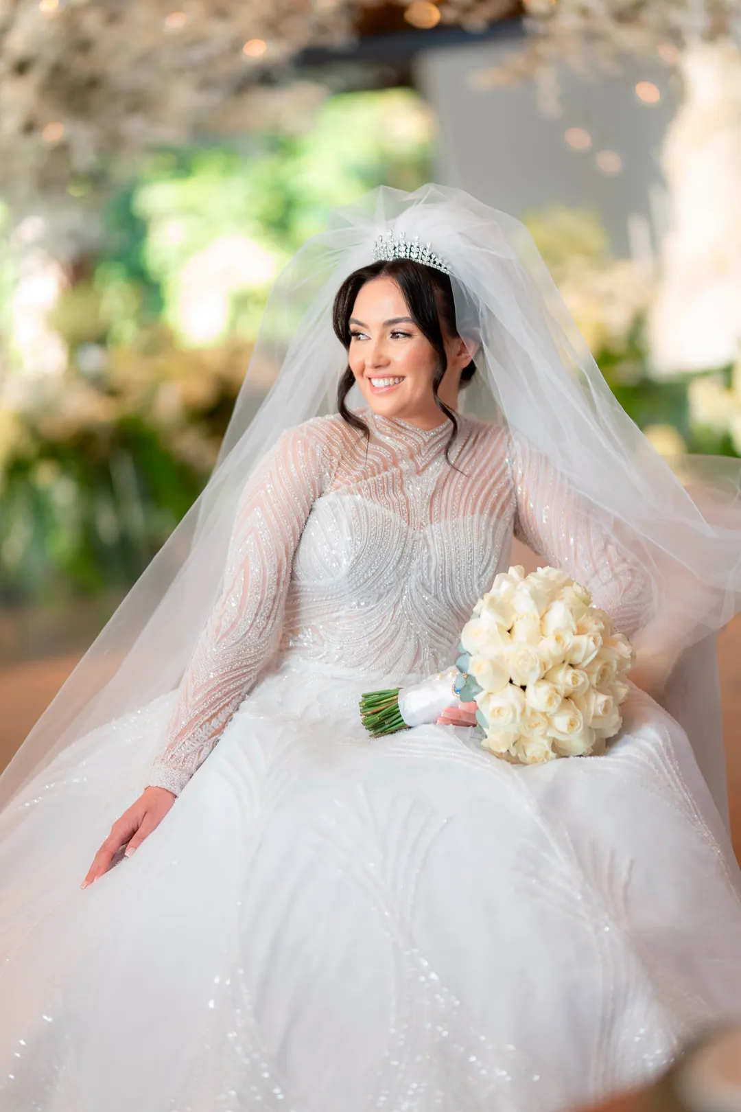 Retrato da noiva sentada com buquê branco, vestido de renda e véu longo