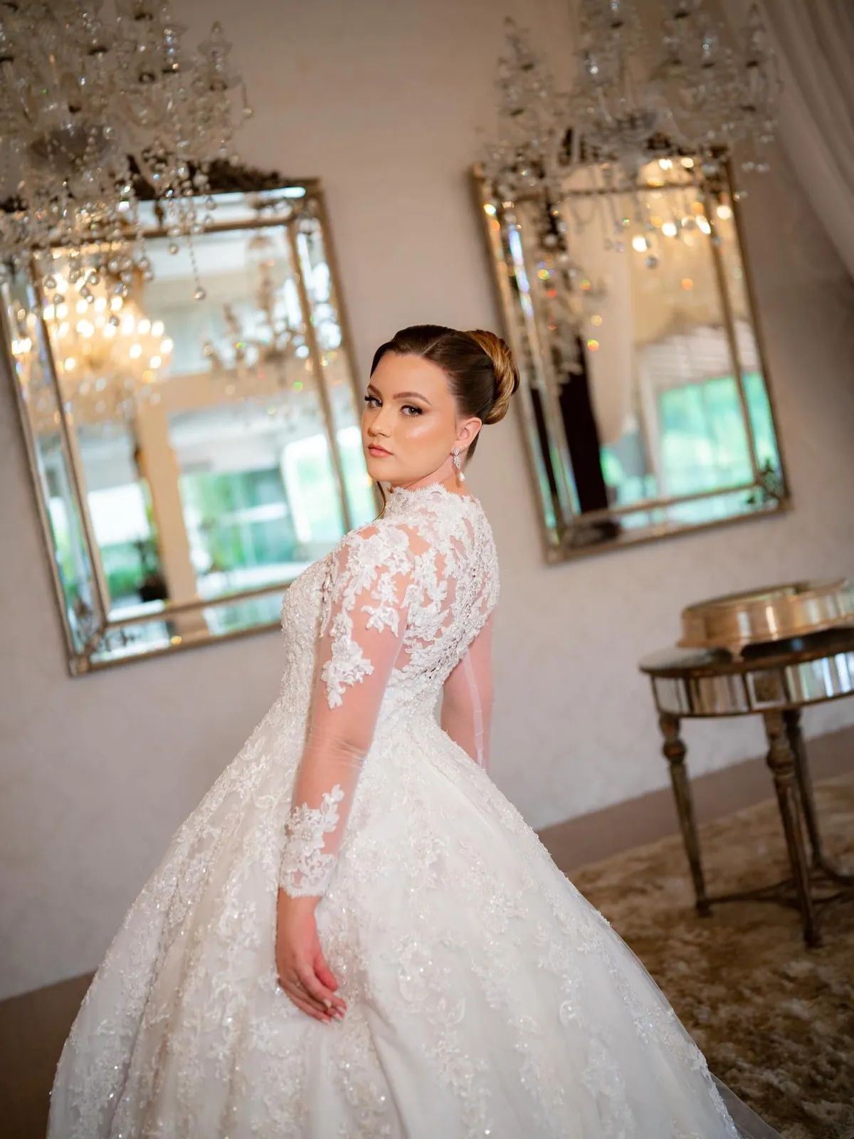 Noiva clássica em vestido de renda de manga longa, em salão de espelhos e lustres de cristal
